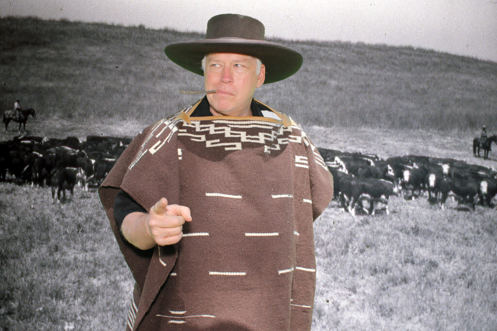 Man klädd som Clint Eastwood cowboy framför en svartvit bild av en massa kor.